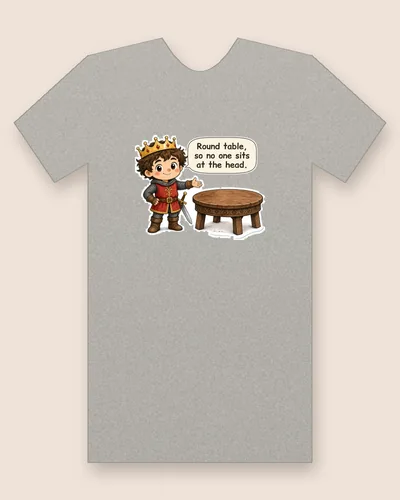 Camelot's King tee mockup: A young king in a gold crown and chain mail showing off a round wooden table, saying “Round table, so no one sits at the head.”